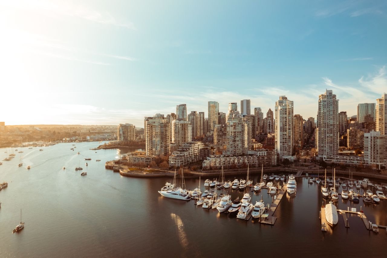 A panoramic view of Vancouvers skyline and marina at sunset, showcasing high-rise buildings and boats.